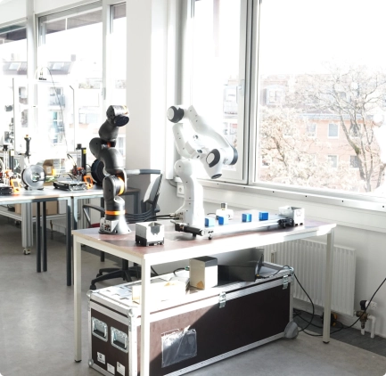 Techniklabor mit modernen Roboterarmen und Arbeitsplätzen vor großen Fenstern mit Blick auf die Umgebung.