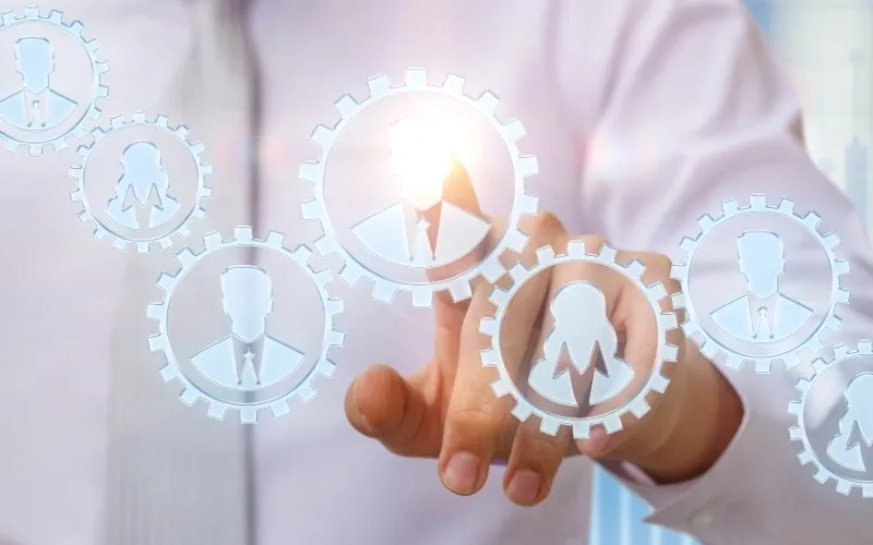 Businessmann interagiert mit virtuellen Zahnrädern, die vernetzte Fachkräfte im Human Resources Management symbolisieren.